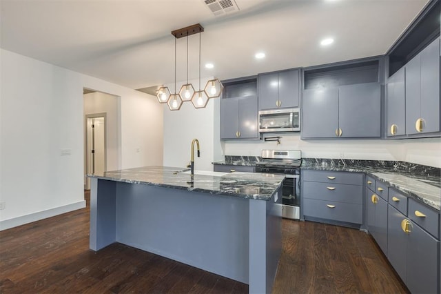 kitchen with stainless steel appliances, a kitchen island with sink, dark wood-type flooring, sink, and hanging light fixtures