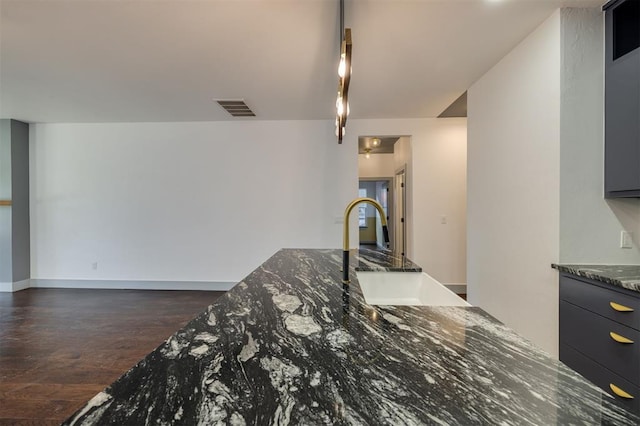 kitchen featuring dark wood-type flooring, dark stone counters, and sink