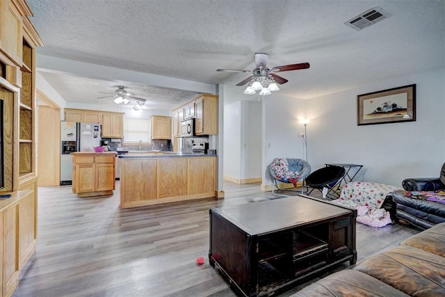 living room featuring ceiling fan, sink, a textured ceiling, and light wood-type flooring