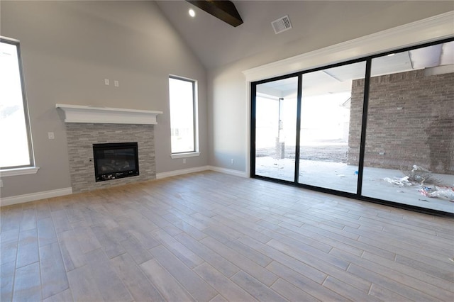 unfurnished living room with a stone fireplace, high vaulted ceiling, and light wood-type flooring