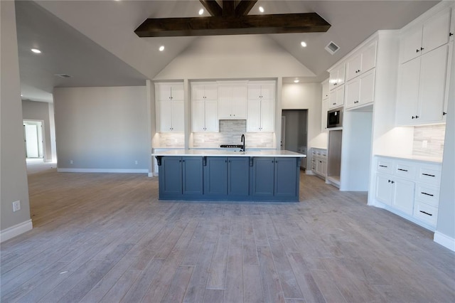 kitchen featuring built in microwave, light hardwood / wood-style flooring, white cabinets, and a center island with sink