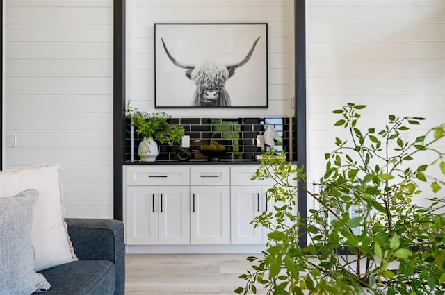 bar with white cabinets, decorative backsplash, and light hardwood / wood-style floors