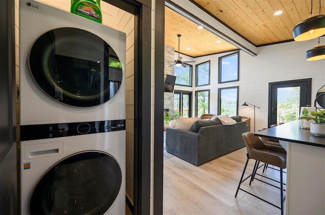 laundry area featuring a towering ceiling, ceiling fan, light hardwood / wood-style flooring, wooden ceiling, and stacked washer and clothes dryer