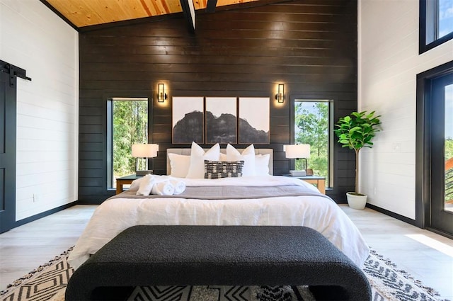 bedroom featuring a barn door, light hardwood / wood-style floors, multiple windows, and wooden walls