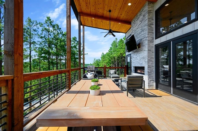 wooden terrace featuring an outdoor stone fireplace and ceiling fan