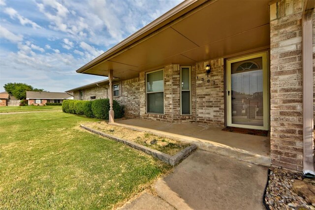 view of exterior entry featuring a lawn and covered porch