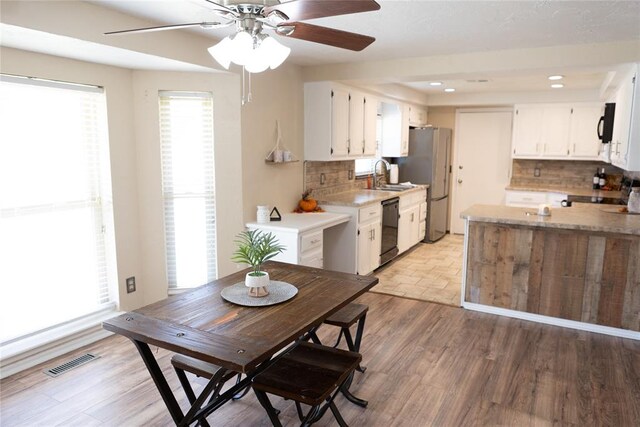 kitchen with white cabinets, light wood-type flooring, tasteful backsplash, and black appliances