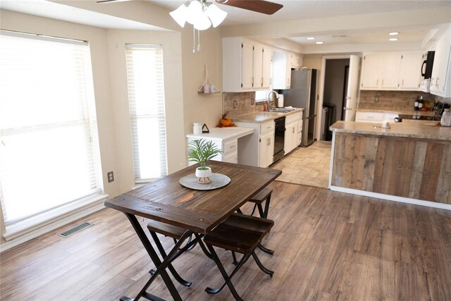 kitchen with black appliances, white cabinets, tasteful backsplash, and light hardwood / wood-style flooring