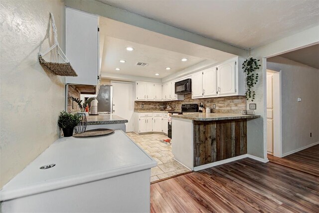 kitchen featuring white cabinetry, light hardwood / wood-style flooring, kitchen peninsula, decorative backsplash, and black appliances