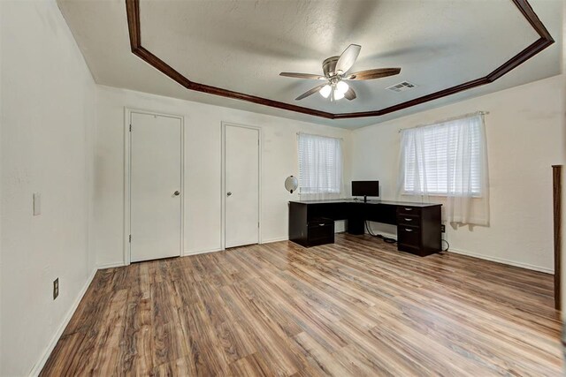 unfurnished office featuring light wood-type flooring, a raised ceiling, ceiling fan, and ornamental molding