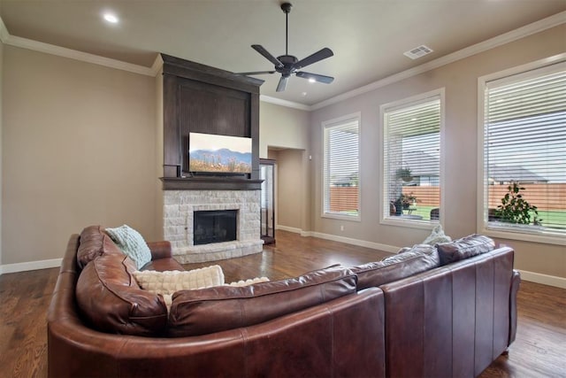 living room with wood-type flooring, a stone fireplace, ceiling fan, and crown molding