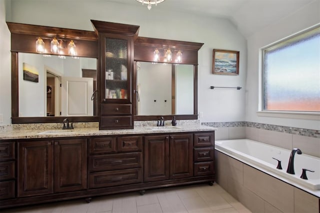 bathroom with tile patterned flooring, vanity, lofted ceiling, and tiled tub