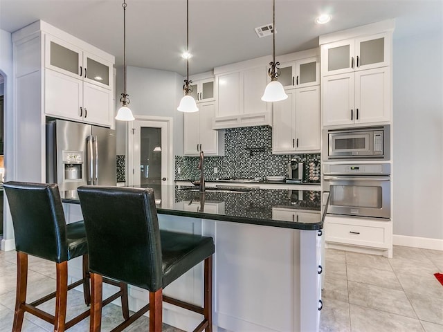 kitchen with hanging light fixtures, an island with sink, a kitchen bar, white cabinets, and appliances with stainless steel finishes