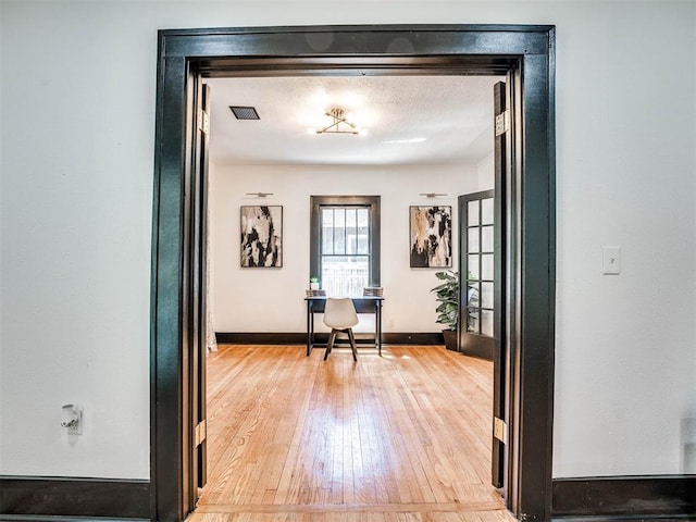 hall with french doors, a textured ceiling, and light wood-type flooring