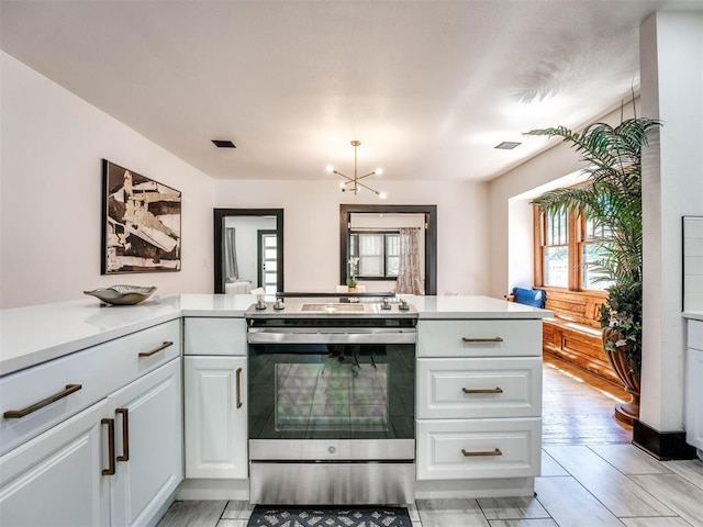 kitchen featuring kitchen peninsula, light hardwood / wood-style flooring, white cabinets, a chandelier, and stainless steel electric range