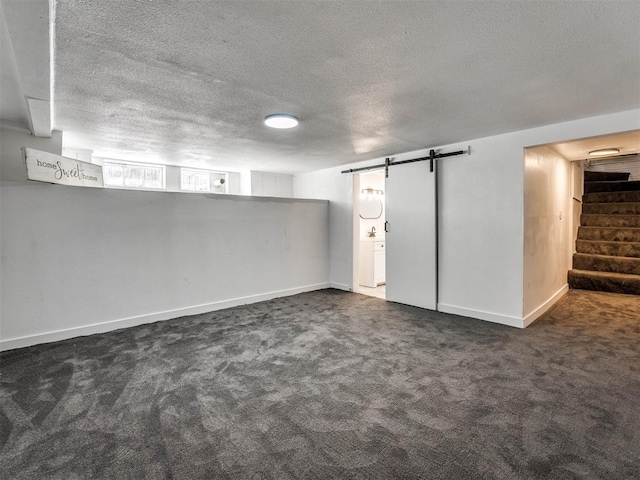 basement with a barn door, a textured ceiling, and dark colored carpet