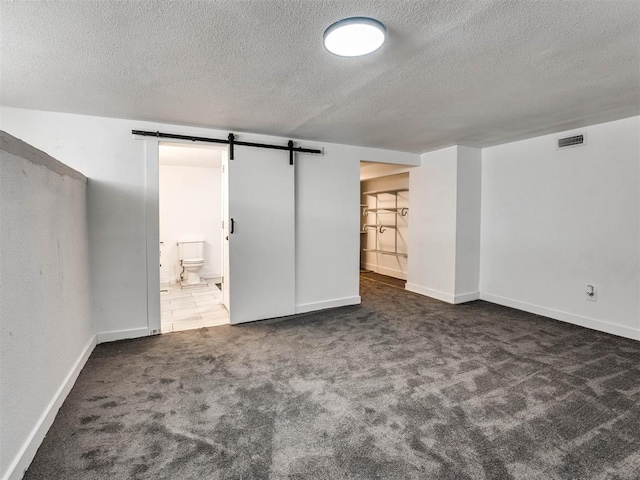 interior space featuring dark colored carpet, a barn door, and a textured ceiling