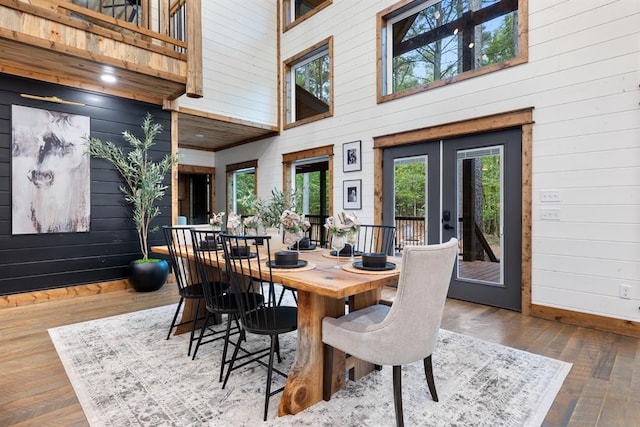 dining area featuring hardwood / wood-style floors, a towering ceiling, french doors, and wood walls