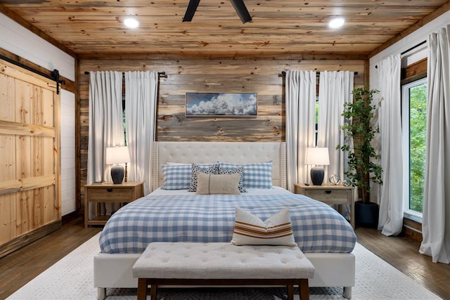 bedroom with a barn door, wooden walls, wood ceiling, and dark hardwood / wood-style floors