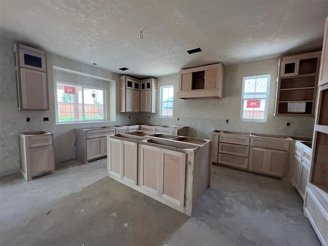 kitchen featuring a wealth of natural light, a center island, a textured ceiling, and light brown cabinetry