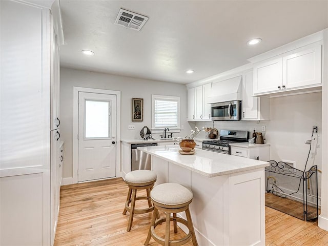 kitchen featuring a kitchen breakfast bar, white cabinetry, light wood-type flooring, and appliances with stainless steel finishes