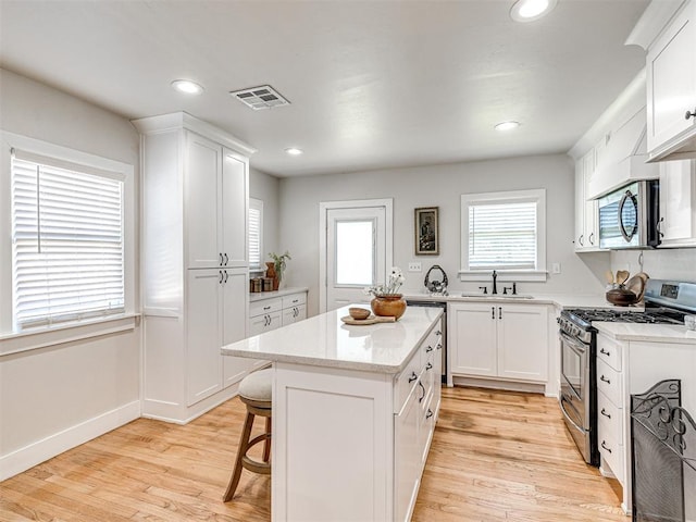 kitchen with a center island, sink, light hardwood / wood-style floors, white cabinets, and appliances with stainless steel finishes