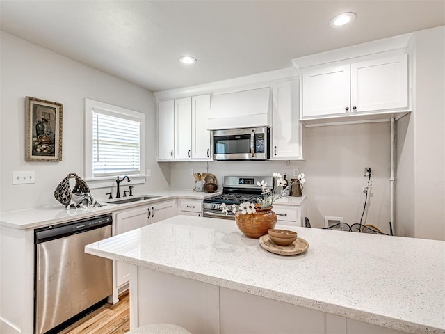 kitchen with light wood-type flooring, light stone counters, stainless steel appliances, sink, and white cabinetry