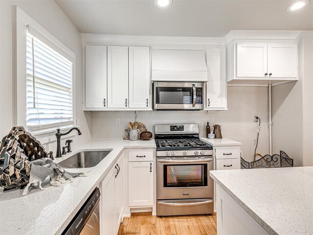 kitchen with light stone countertops, light hardwood / wood-style flooring, white cabinets, and stainless steel appliances