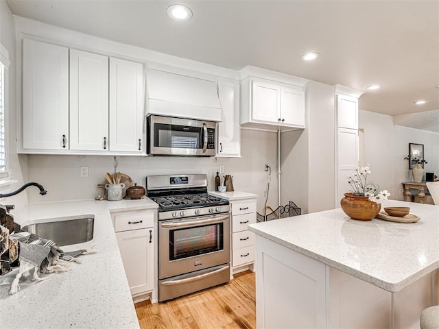 kitchen featuring sink, light stone counters, appliances with stainless steel finishes, white cabinets, and light wood-type flooring