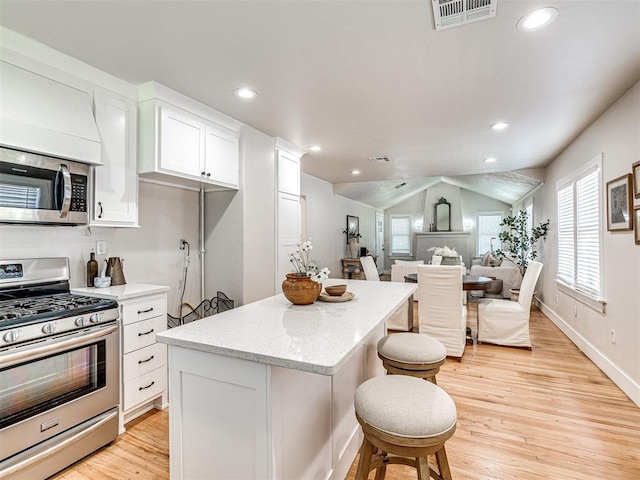 kitchen featuring light wood-type flooring, stainless steel appliances, vaulted ceiling, white cabinets, and a center island