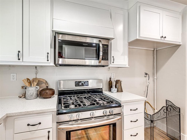 kitchen with light stone countertops, stainless steel appliances, white cabinets, and hardwood / wood-style flooring