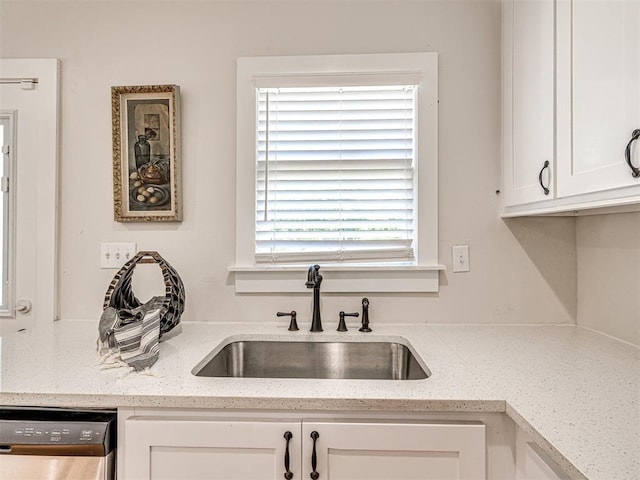 kitchen with light stone counters, white cabinetry, stainless steel dishwasher, and sink