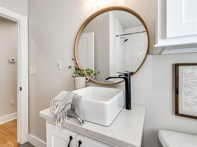 bathroom featuring a tile shower, hardwood / wood-style floors, vanity, and toilet