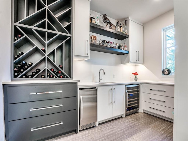 interior space with wine cooler, sink, white cabinets, and light wood-type flooring