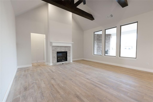 unfurnished living room with beam ceiling, high vaulted ceiling, a fireplace, and light hardwood / wood-style floors