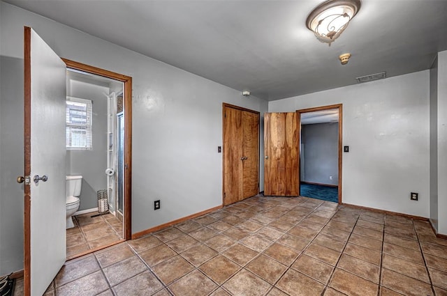 unfurnished bedroom featuring ensuite bathroom, a closet, and light tile patterned floors