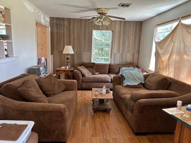 living room with a textured ceiling, hardwood / wood-style flooring, ceiling fan, and wood walls