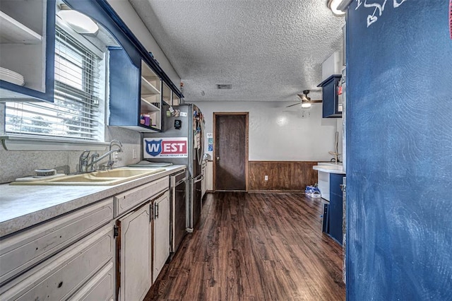 kitchen featuring dishwasher, dark wood-type flooring, blue cabinets, a textured ceiling, and wooden walls