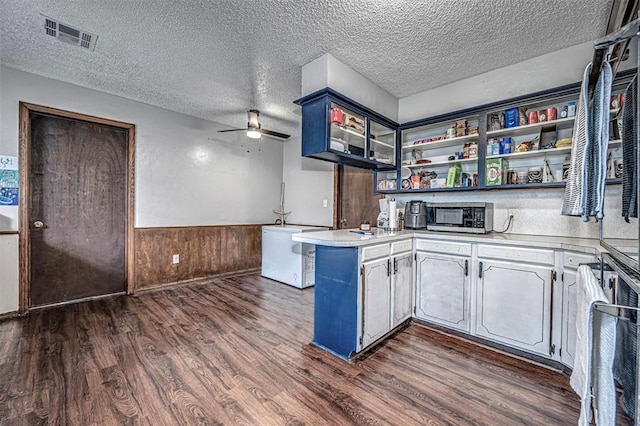 kitchen featuring wood walls, blue cabinetry, a textured ceiling, dark hardwood / wood-style flooring, and kitchen peninsula