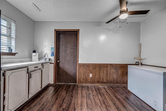 kitchen with a textured ceiling, fridge, dark wood-type flooring, and wood walls