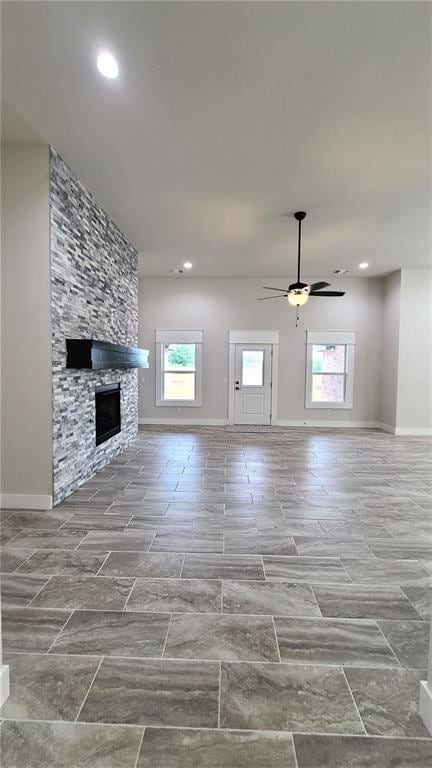 unfurnished living room with ceiling fan and a stone fireplace