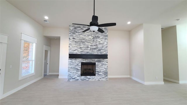 unfurnished living room with light hardwood / wood-style flooring, a stone fireplace, and ceiling fan