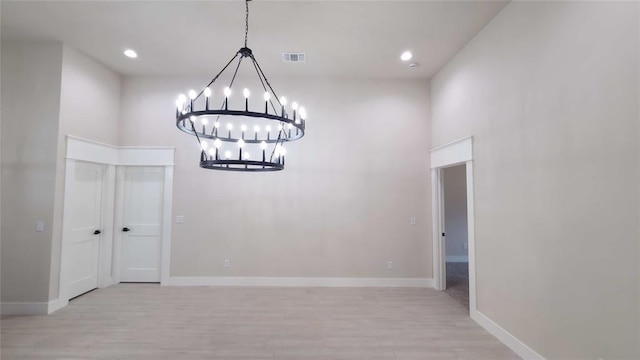 unfurnished dining area with a towering ceiling, light hardwood / wood-style flooring, and a notable chandelier