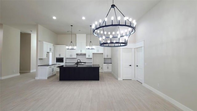 kitchen with sink, backsplash, an island with sink, white cabinets, and light wood-type flooring