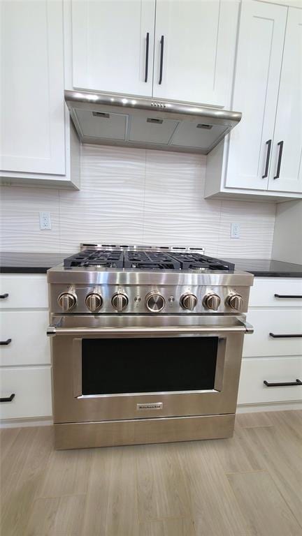 kitchen with white cabinets, light wood-type flooring, backsplash, and stainless steel range