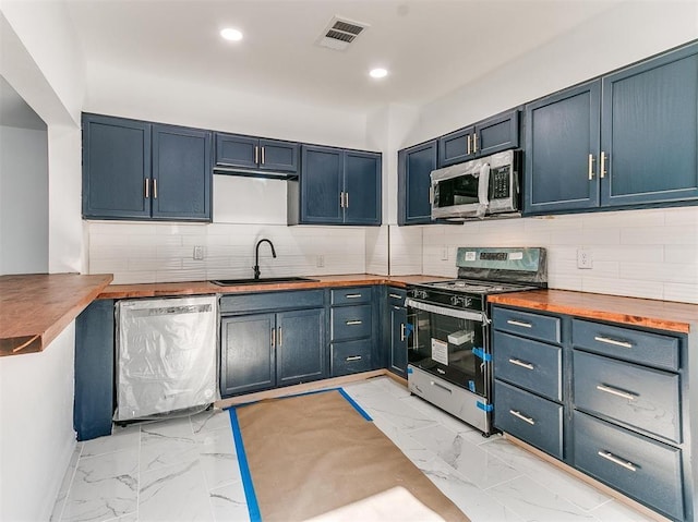 kitchen with wooden counters, appliances with stainless steel finishes, decorative backsplash, sink, and blue cabinetry