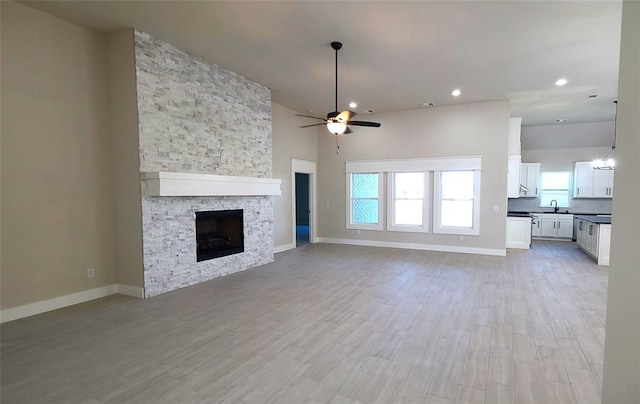 unfurnished living room featuring ceiling fan, sink, a high ceiling, a stone fireplace, and light hardwood / wood-style flooring