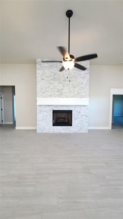 unfurnished living room with a stone fireplace and ceiling fan