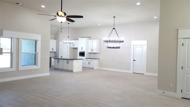 kitchen with a kitchen island, light wood-type flooring, white cabinetry, and high vaulted ceiling