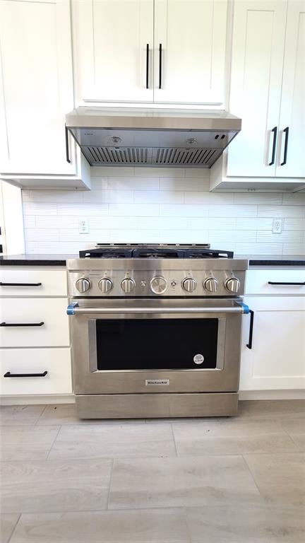 kitchen with backsplash, white cabinets, high end range, and extractor fan